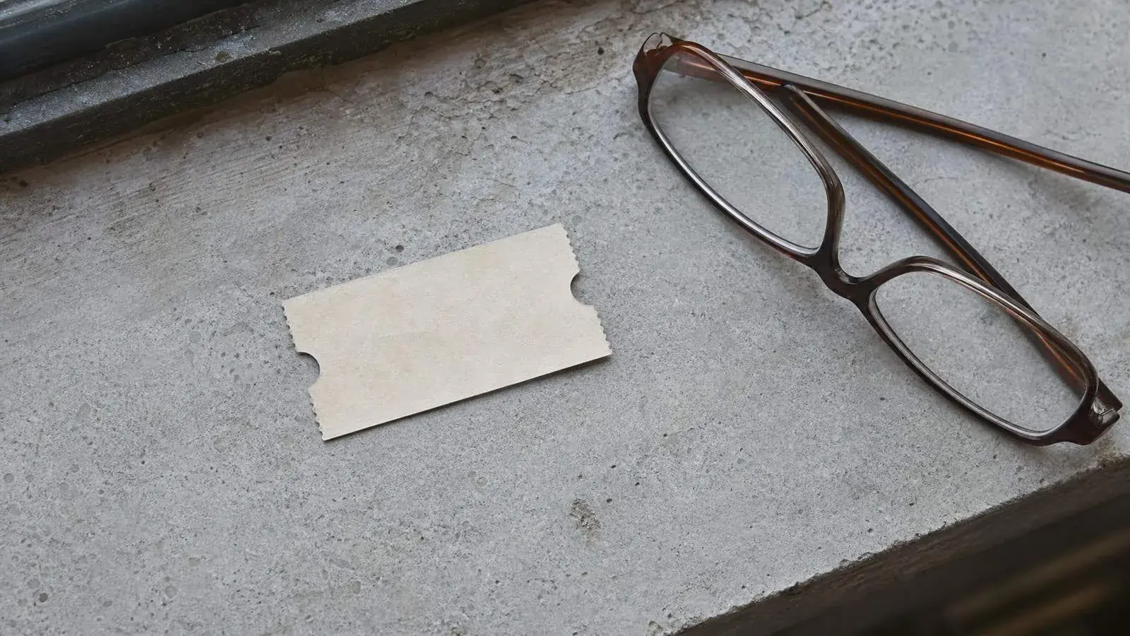 A blank paper ticket lying on a worn stone ledge beside reading glasses