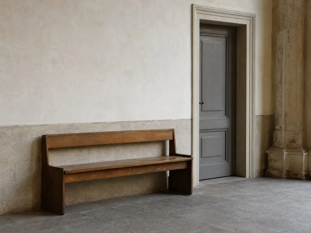 An empty wooden bench against a plastered wall beside a closed door