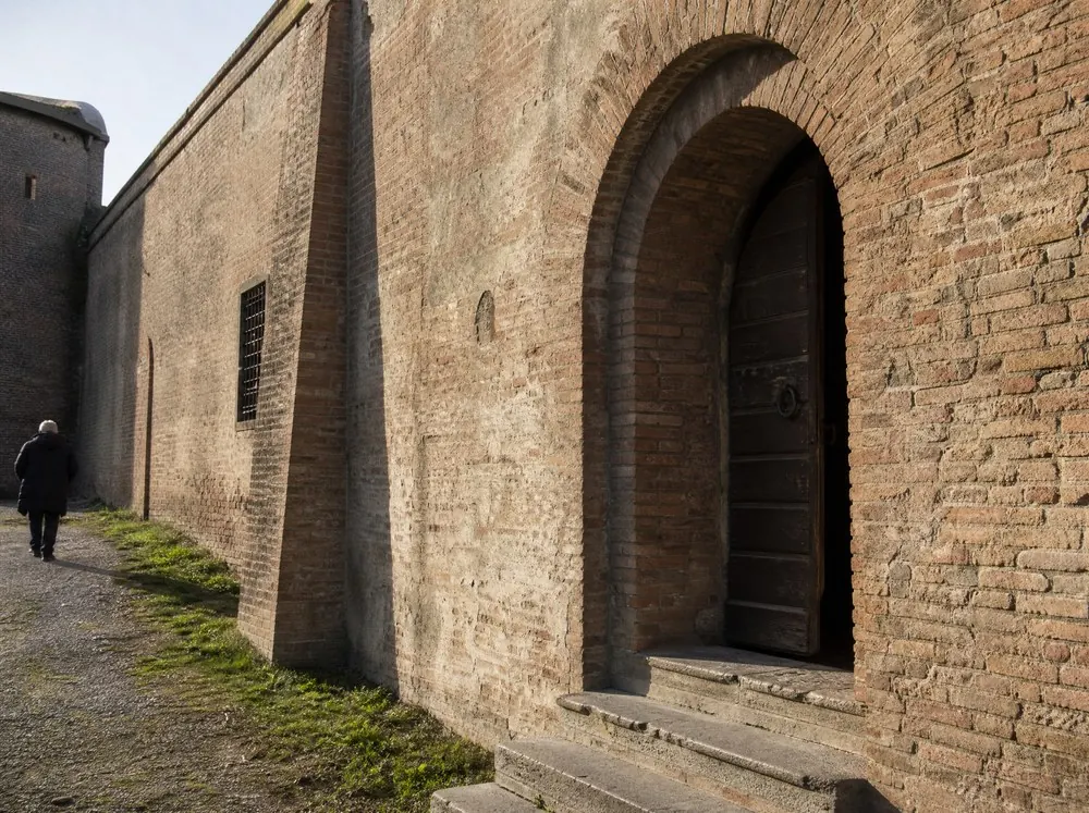 A deep arched brick portal with worn stone steps and a timber door standing ajar