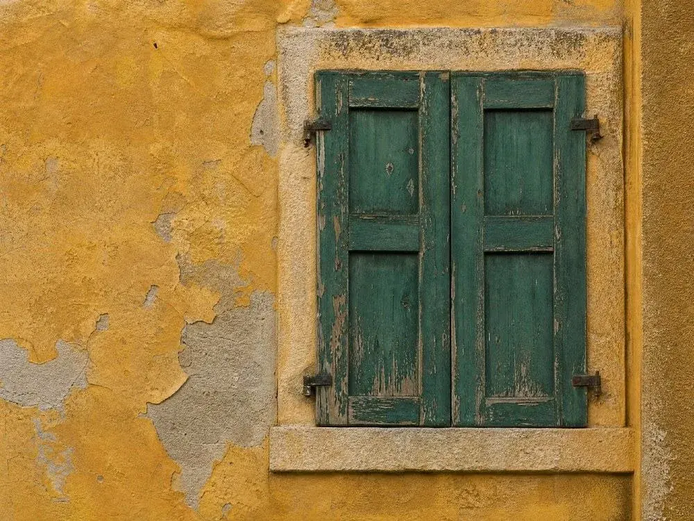 Weathered green shutters closed against an ochre rendered wall